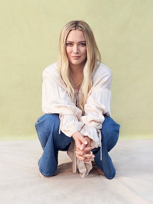 Hilary Duff crouching in a white Tove top, Coach vest and jeans,Astrid & Miyu earrings and Jimmy Cho...